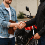 Aproximação de duas pessoas dando um aperto de mão, uma delas segurando as chaves de uma moto, simbolizando negociação, venda ou transferência de bens em economia pessoal.